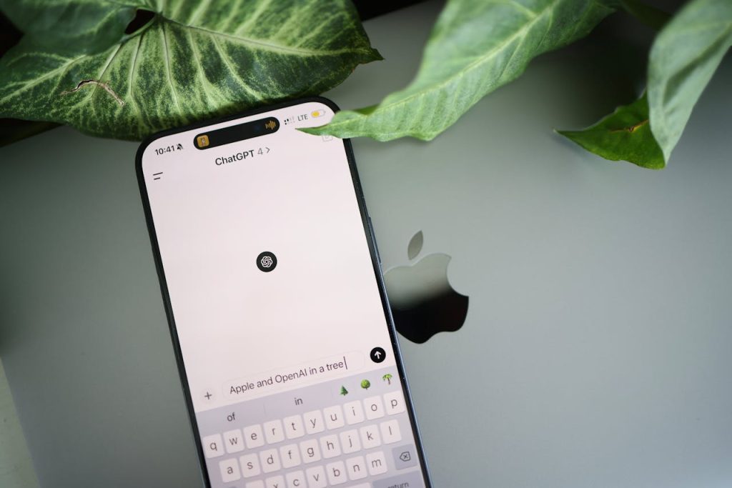 close-up-of-a-smartphone-displaying-chatgpt-20870794 A smartphone shows a ChatGPT interface placed on an Apple laptop in a leafy environment.