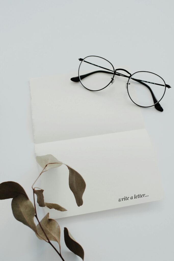 A minimalist flat lay featuring eyeglasses, eucalyptus leaves, and open letter with text.